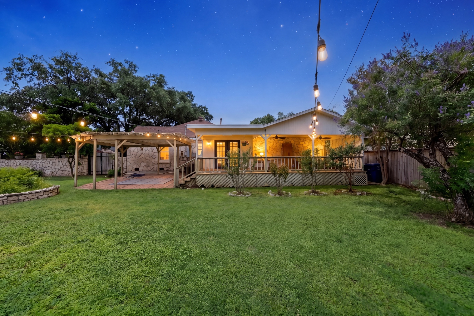 Night view of the backyard lawn, lit deck, and pergola at Casa Thorman