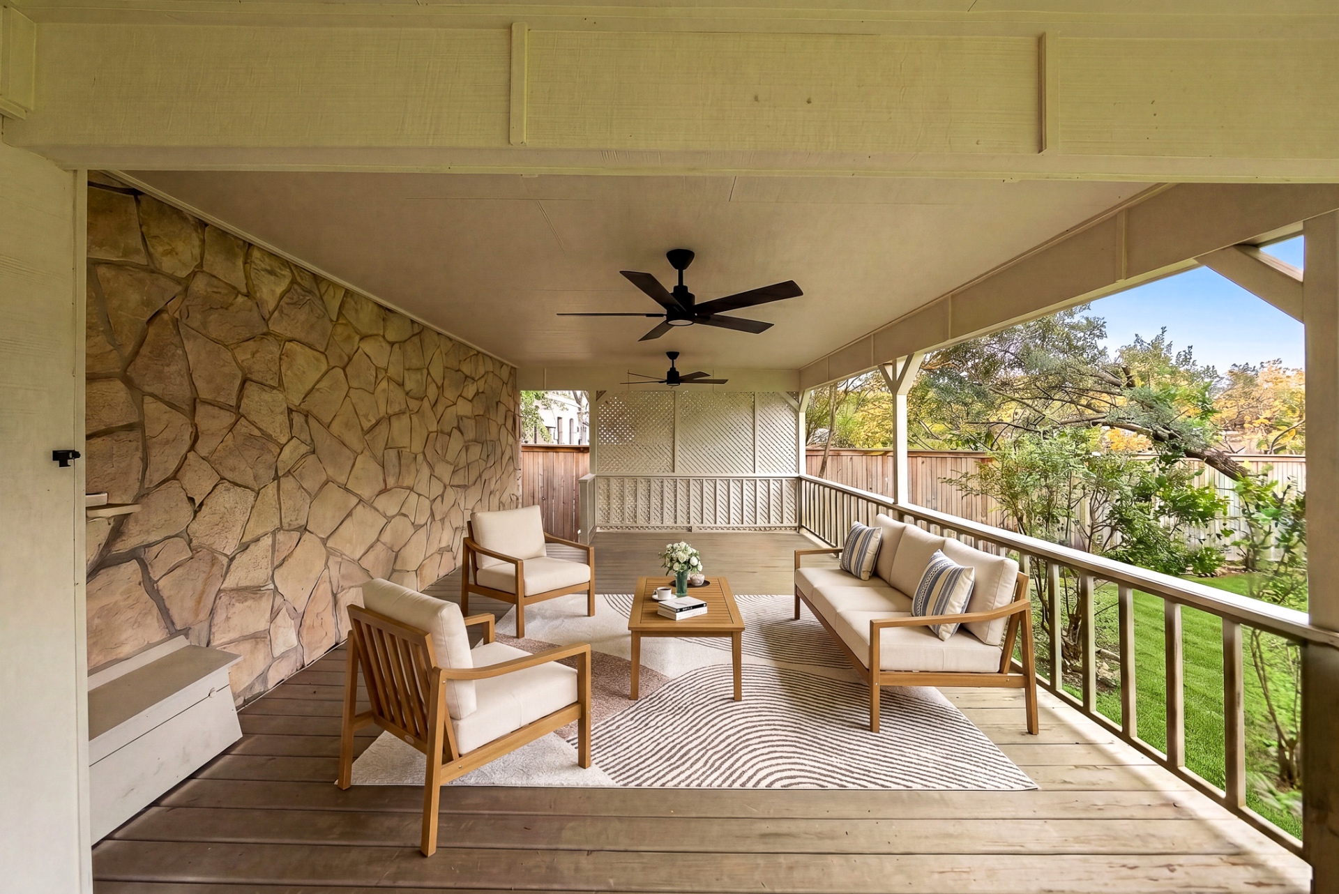 Covered back deck with stone wall, lounge seating, and ceiling fans at Casa Thorman